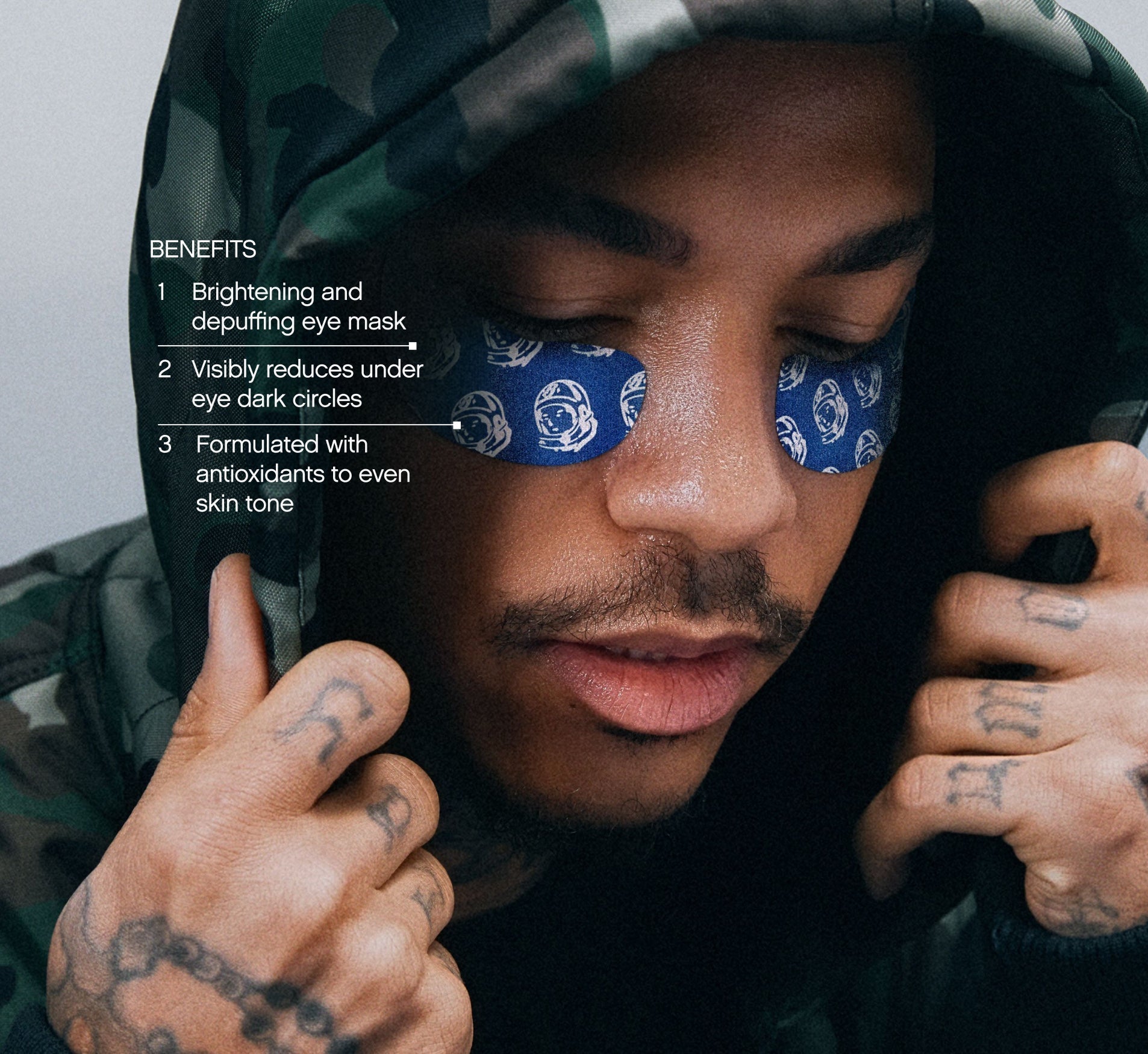 Eye patches for puffiness from Topicals shown applied across both eyes of a tattooed man in a camo hoodie, with benefits callouts for dark circle reduction and skin tone evening.